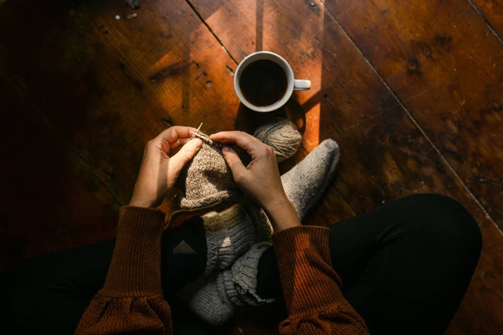 personne assise en tailleur en train de tricoter devant une tasse de café