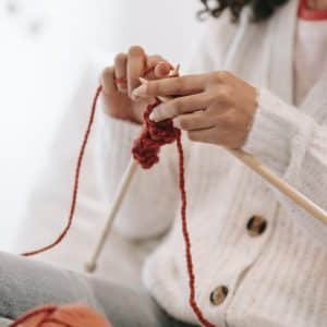 dame assise vêtu d'un cardigan tricoté blanc et qui tricote