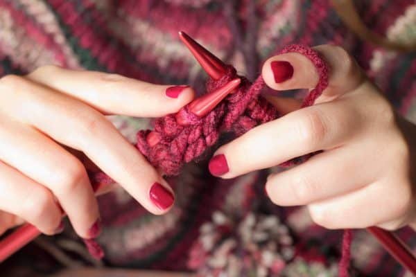 mains qui tricotent un ouvrage rouge